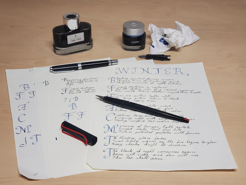 Photo of fountain pens, ink, and pages of calligraphy